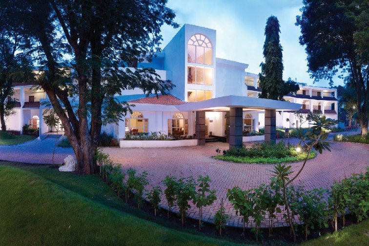 Hotel Exterior - Sasan Gir Beautiful exterior of a hotel in Sasan Gir, showcasing its well-maintained gardens, modern architecture, and welcoming entrance, illuminated in the evening.