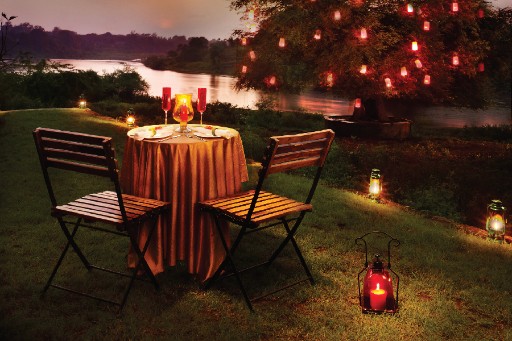 Romantic Dining - Sasan Gir Romantic outdoor dining setup by the river in Sasan Gir, with a candlelit table for two, surrounded by nature and serene water views.